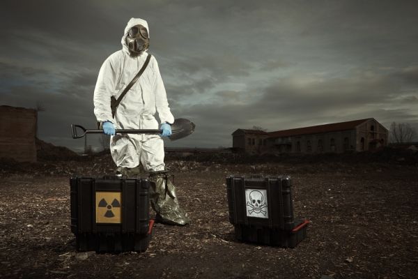 Person in hazmat gear and gas mask with a shovel